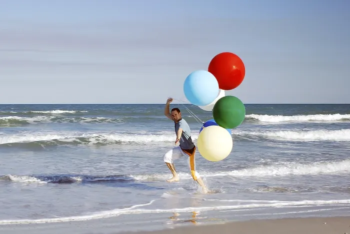 Framed Print : Young man with large colourful balloons at the beach