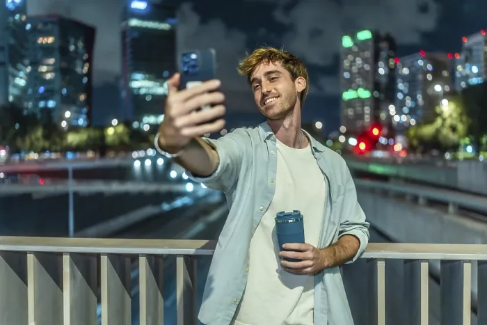Framed Print : Young man smiling and taking a selfie with a smartphone while holding a reusable coffee cup