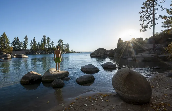 Framed Print : Young man in swimming trunks standing on a round stone in the water