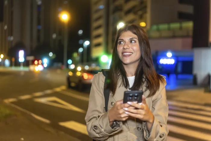 Framed Print : Young woman smiling and looking away while using a mobile phone on a pedestrian crossing