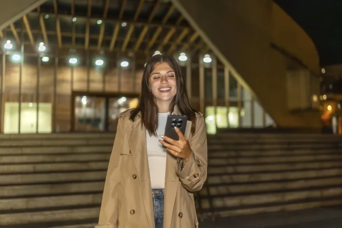 Framed Print : Young woman smiling while looking at her mobile phone outdoors