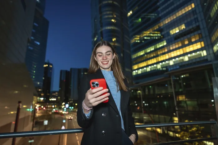 Framed Print : Young woman smiling while reading content on her red smartphone Framed Print : Young woman smiling while reading content on her red smartphone