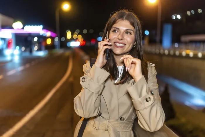 Framed Print : Young woman in a trench coat smiling happily while having a phone call