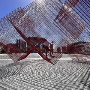 Abstract red metal sculpture with sunburst in urban space