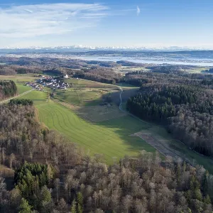 Aerial view of fields and forests with a village in the distance and mountains in the background