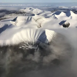 Aerial view, mountain peak with snow above cloud cover Aerial view, mountain peak with snow above cloud cover