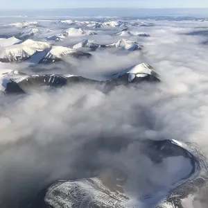 Aerial view, mountain peak with snow above cloud cover Aerial view, mountain peak with snow above cloud cover