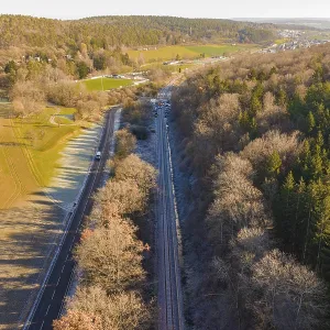 Aerial view of a railway line between trees and a road in a rural area Aerial view of a railway line between trees and a road in a rural area
