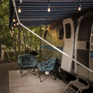 An Airstream camper trailer with string lights and chairs set up in a forest