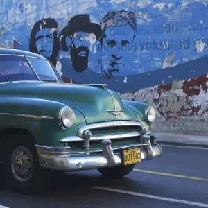 American vintage cars as a Cuban taxi driving along a wall with paintings of Fidel Castro and Che Guevara American vintage cars as a Cuban taxi driving along a wall with paintings of Fidel Castro and Che Guevara