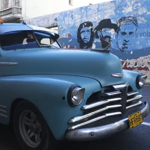American vintage cars as a Cuban taxi driving along a wall with paintings of Fidel Castro and Che Guevara