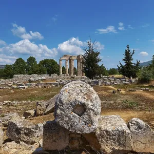 Ancient temple columns in an open field with surrounding trees and mountains in the background