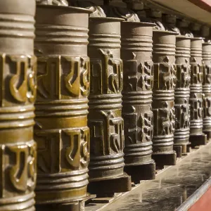 Artfully decorated metal prayer wheels in a row in a monastic setting with intensive play of light and shadow Artfully decorated metal prayer wheels in a row in a monastic setting with intensive play of light and shadow
