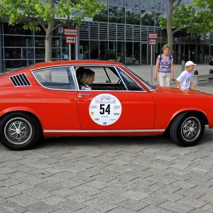 AUDI 100 Coupe S, red classic car in a city environment surrounded by people and modern architecture