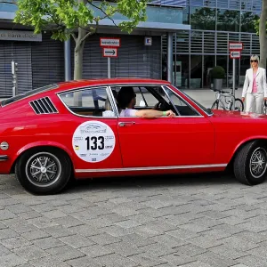 AUDI, A red classic car in profile stands on a cemented square surrounded by trees