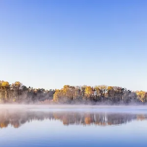Autumn colors on the trees at a lake with water reflections and mist Autumn colors on the trees at a lake with water reflections and mist