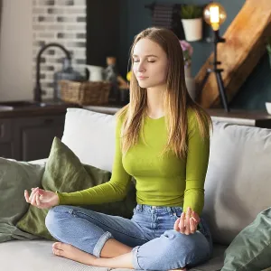 barefoot woman sitting on sofa in Lotus pose and meditating during yoga session at home