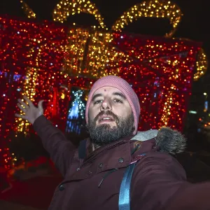 Bearded man taking a selfie in front of giant luminous christmas gift box in bayonne Bearded man taking a selfie in front of giant luminous christmas gift box in bayonne