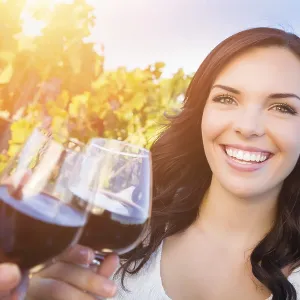 Beautiful young adult woman enjoying glass of wine tasting toast in the vineyard with friends
