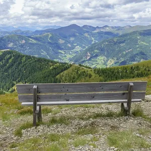 An empty bench with a view of a vast mountain landscape under cloudy sky