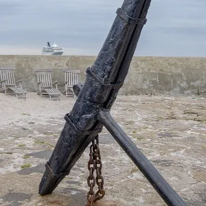 Big old anchor on a rocky coast with a cruise ship on the horizon