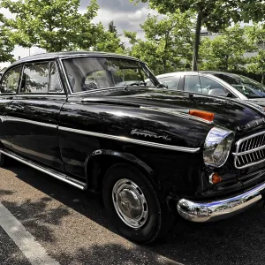 A black classic car is parked in a parking lot surrounded by trees and modern cars A black classic car is parked in a parking lot surrounded by trees and modern cars