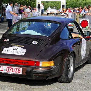 Black Porsche at a classic car rally surrounded by spectators and green trees