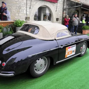 Black Porsche convertible with beige soft top drives relaxed through the old town at a classic car rally Black Porsche convertible with beige soft top drives relaxed through the old town at a classic car rally