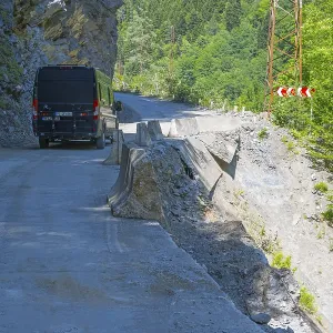 A black van drives on a remote road along a steep cliff with green vegetation A black van drives on a remote road along a steep cliff with green vegetation