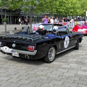 Black vintage convertible with racing stickers at a car event on a paved road