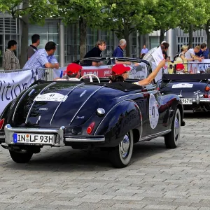 Two black vintage convertibles on a street surrounded by a crowd
