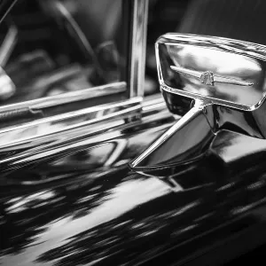 Black and white image of a vintage Ford Thunderbird chrome side mirror reflecting light in St