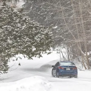 A blue car travels down a snow-covered road in a forest