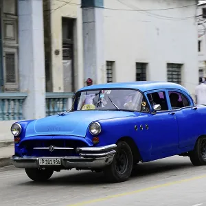 Blue classic car on a road surrounded by colonial architecture