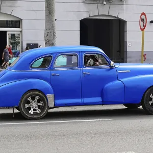Blue classic car on an urban street in front of a building with windows