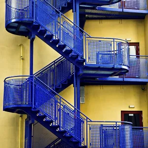 Blue metal fire escape staircases against a yellow wall creating a stark industrial contrast