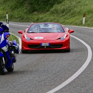 Blue motorbike overtakes red Ferrari convertible on winding road Blue motorbike overtakes red Ferrari convertible on winding road