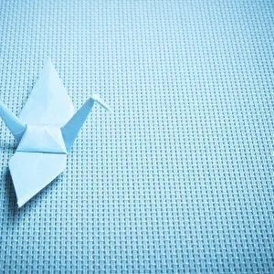 Blue origami crane resting on a woven textured surface Blue origami crane resting on a woven textured surface