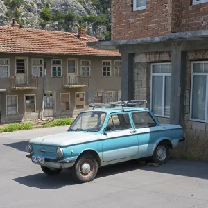 A blue retro car parked in front of dilapidated buildings under a clear sky A blue retro car parked in front of dilapidated buildings under a clear sky
