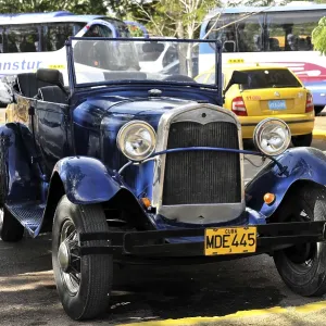 A blue vintage car parked under the sun with its licence plate visible