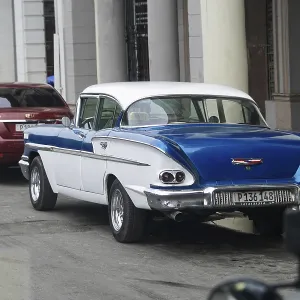 Blue and white classic car parked next to modern cars in the city