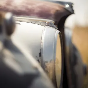 Blurred close-up of an old Jaguar car's headlight and surface with visible rust in rural Huron County