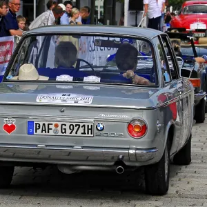 BMW, rear view of a grey classic car at a car event surrounded by people and banners