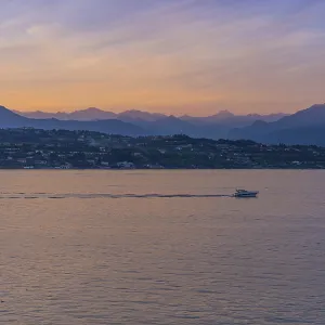 A boat in the sunset with the silhouettes of the mountains in the background on Lake Garda A boat in the sunset with the silhouettes of the mountains in the background on Lake Garda