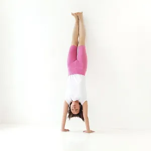 Full body of focused slim female female performing handstand near wall while practicing yoga in light room by