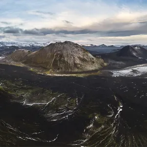 Vue imprenable d'une montagne volcanique entourée de mousses vertes luxuriantes, de rivières sinueuses et de végétation automnale colorée dans les hautes terres isolées d'Islande sous un ciel orageux.
