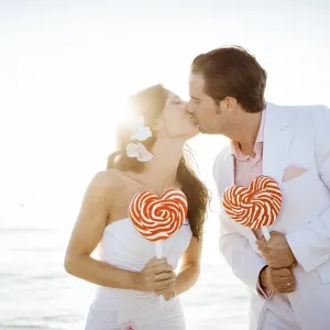 Bride and groom kissing, heart-shaped lollipops in their hands