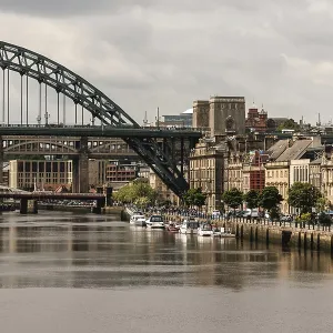 Bridge spanning the Tyne river surrounded by city buildings and moored boats under a cloudy sky in Newcastle Upon Tyne Bridge spanning the Tyne river surrounded by city buildings and moored boats under a cloudy sky in Newcastle Upon Tyne