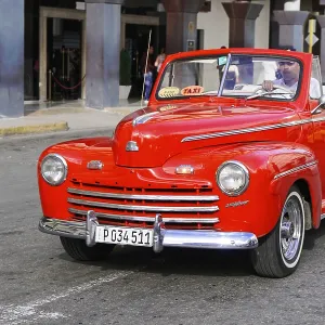 A bright red classic car drives as a taxi through city streets A bright red classic car drives as a taxi through city streets