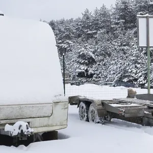 Broken tourist car trailer covered with snow in the winter forest landscape